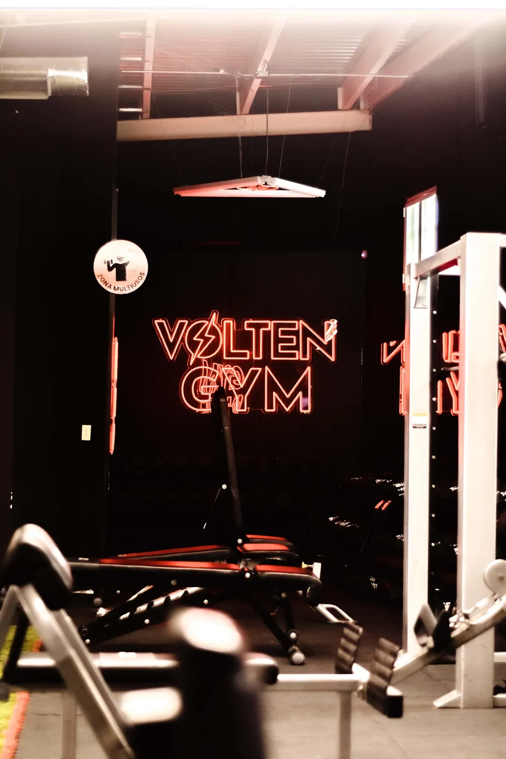 El letrero de neón de Volten Gym junto a una máquina de poleas.
